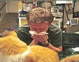 photo of a man sneezing and a cat sitting nearby typical pet allergy