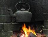 photo of a black cast iron tea pot over a fire in a fireplace brewing a pot of black tea