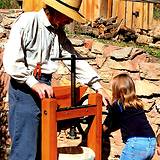a man in a straw hat with little girl operating an apple press for vinegar making
