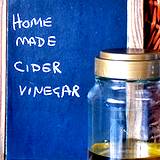 a homemade jar of apple cider vinegar with chalkboard behind it with words home, made, cider, vinegar